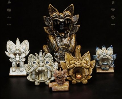 The four ceramic guardians grouped in front of a large bronze-glazed studio piece on black