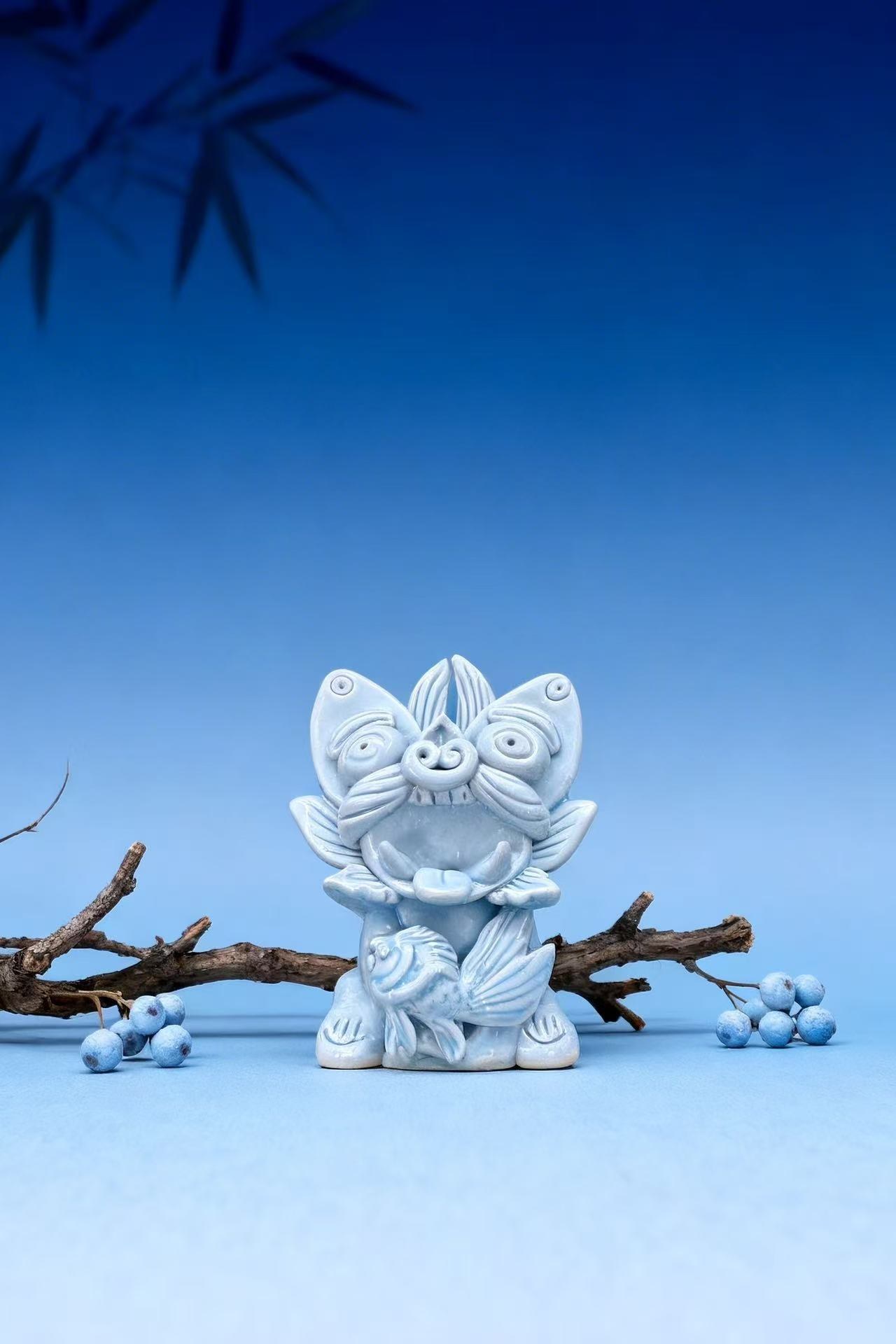 Nachuan ceramic guardian in sky-blue glaze holding a carp, with blueberries, against a blue backdrop