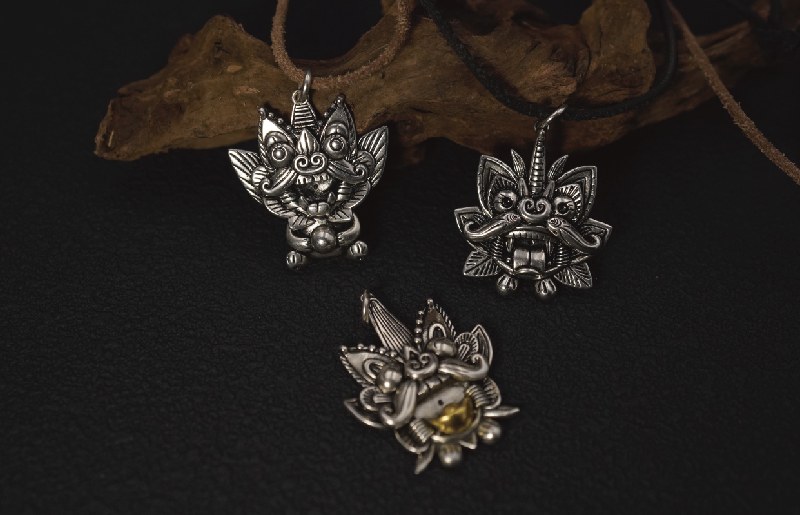Three sterling silver Wamao guardian pendants on leather cords, resting against a piece of driftwood